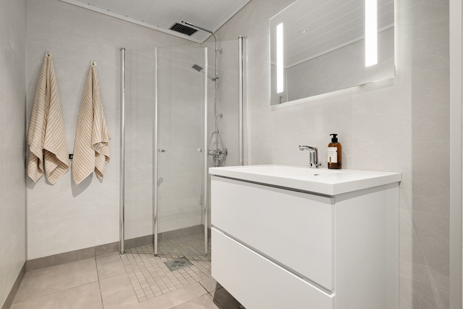Badet er utstyrt med pen vegghengt servantinnredning, dusjhjørne med glassdører og vegghengt toalett. Galleribilde