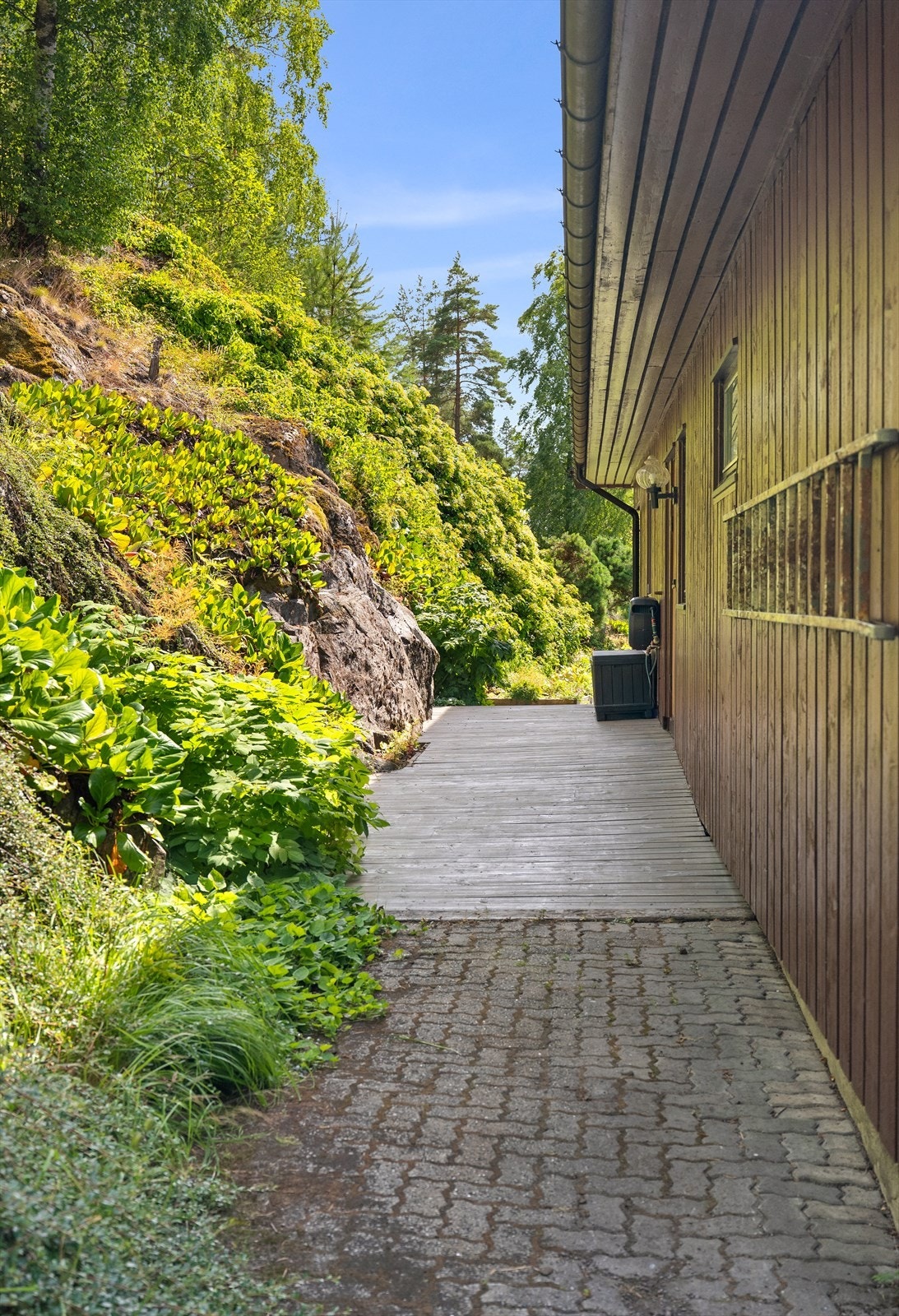 Østsiden av huset vender mot skogen. Egen ytterdør og terrassedør til kjøkkenet på denne siden. Galleribilde