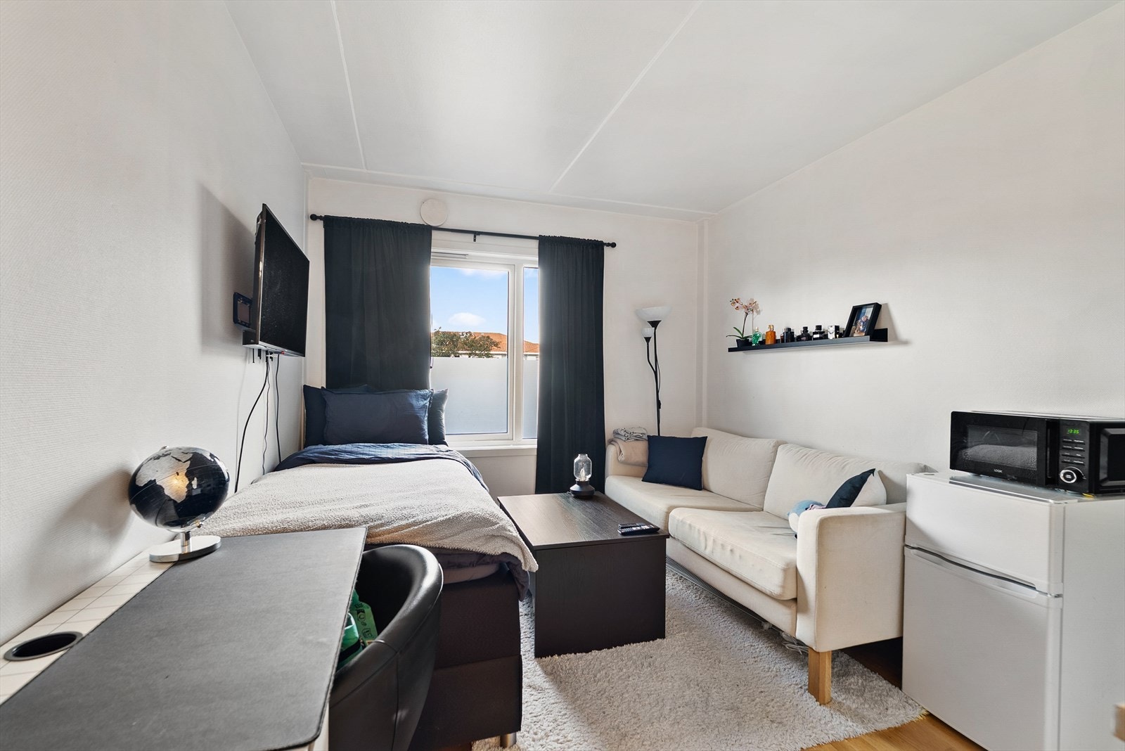 Hybelens oppholdsrom er innredet med plass til både seng, sofa og arbeidsplass. Galleribilde
