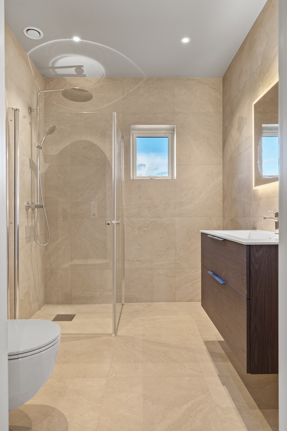 Badet er innredet med romslig dusjsone med glassvegger, moderne baderomsmøbel med god oppbevaringsplass og stort speil med integrert belysning. Galleribilde