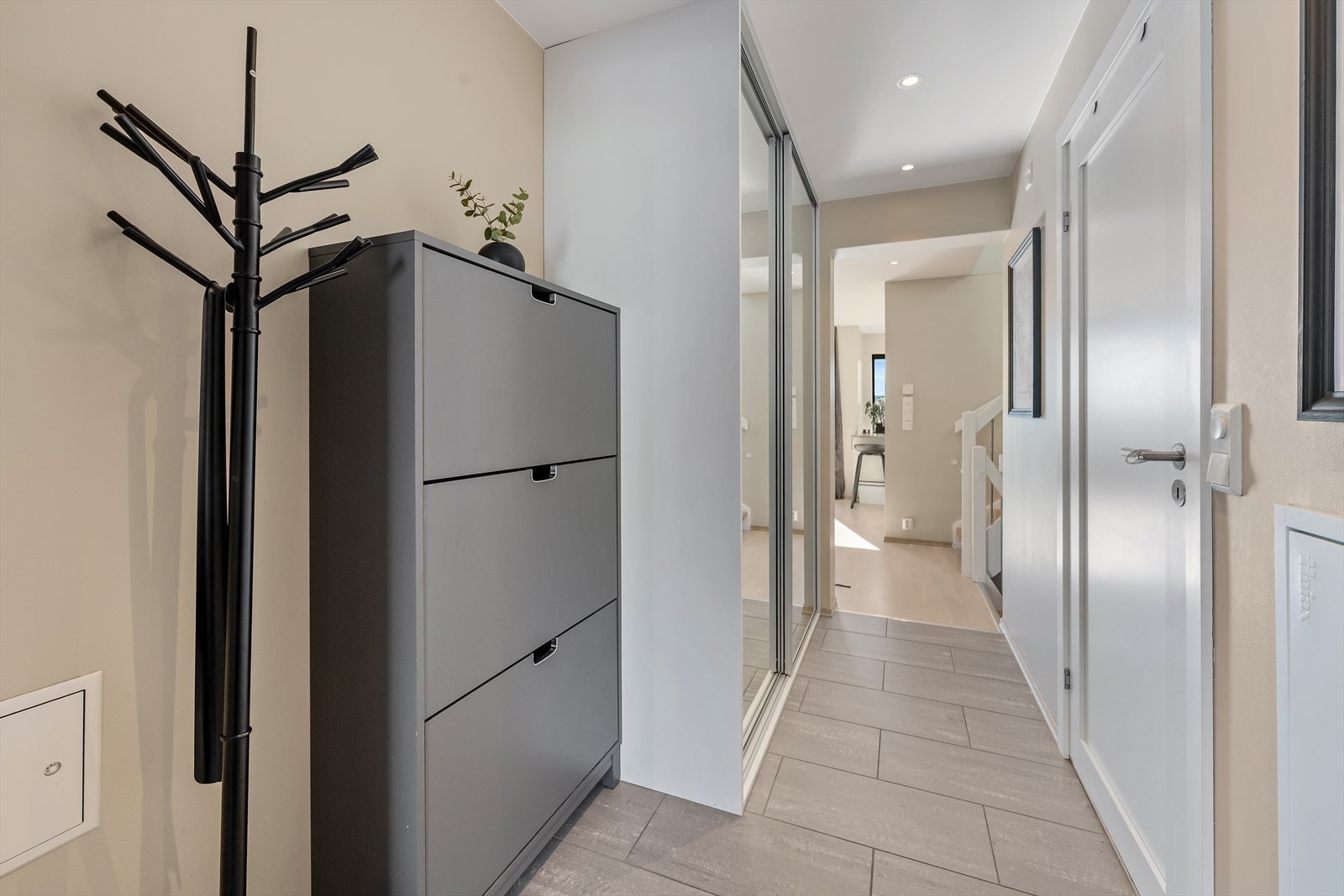Velkommen inn! Entreen er pent innredet med fliser på gulv med underliggende varme, lysmalte vegger, og downlightsbelysning i himling. Det er godt med oppbevaringsplass i skyvedørsgarderobe med speilfronter, samt fin plass til skoskap og knaggrekke Galleribilde