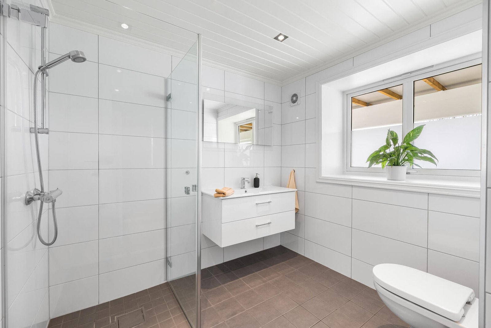 Badet i underetasjen er velholdt og pent, med hvite fliser på veggene, downlights i himlingen og sandfargede fliser på gulv med gulvvarme. Galleribilde