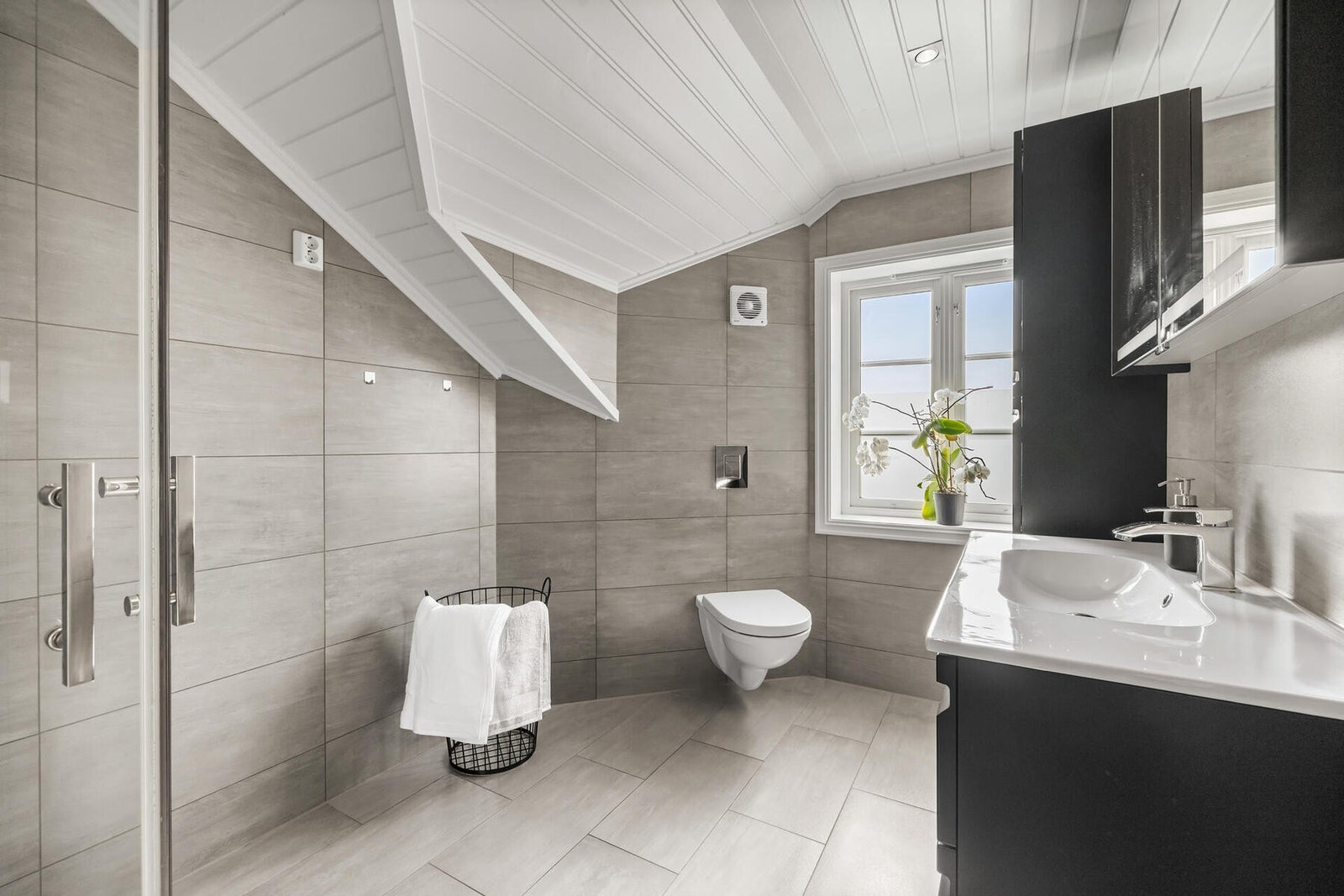 Ved soverommene i loftsetasjen er det et delikat bad med downlights i himlingen, grå fliser på veggene og matchende fliser på gulv med gulvvarme. Galleribilde