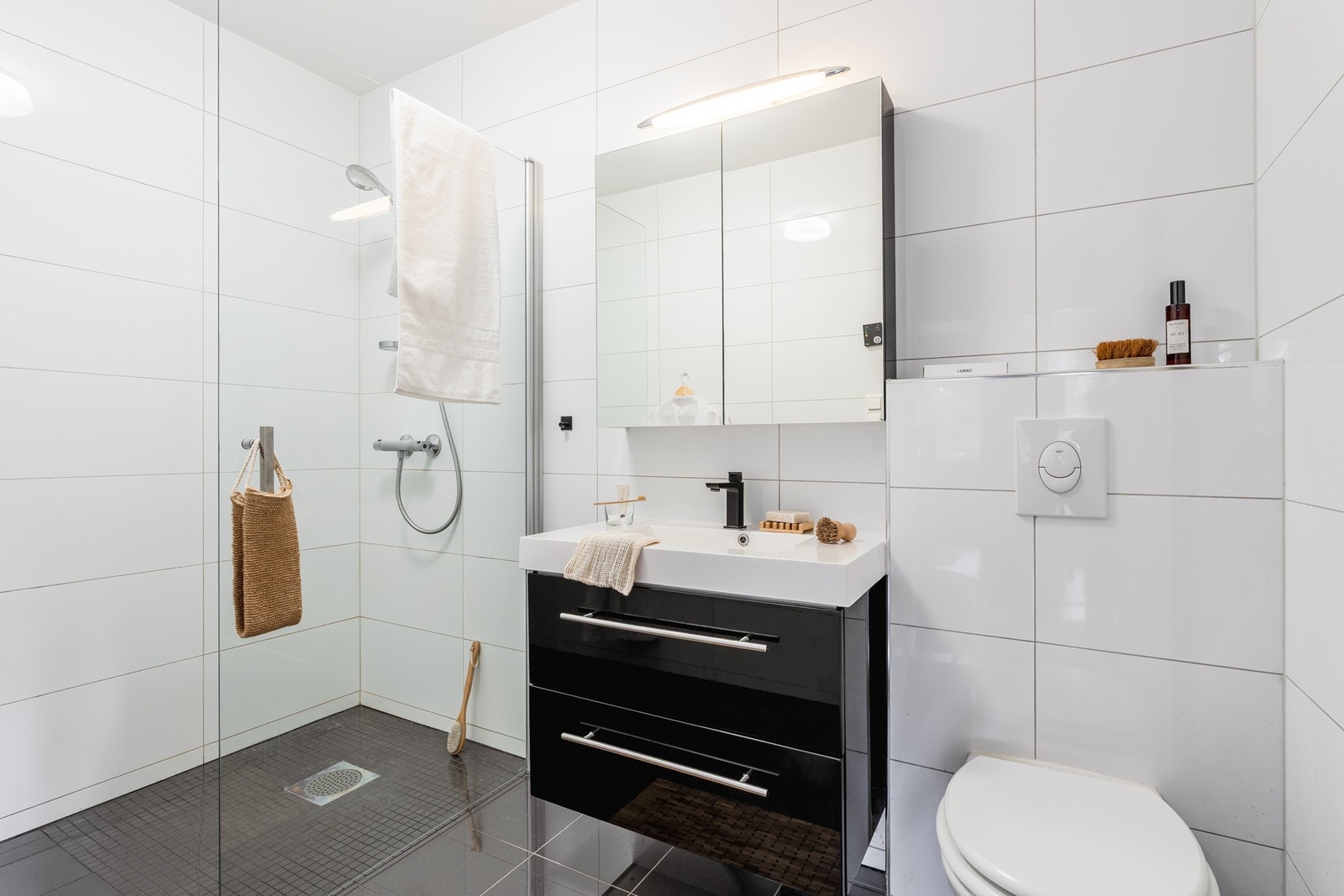 Badet er flislagt med dusjhjørne, vegghengt toalett og skuffeinnredning med overliggende servant. Galleribilde