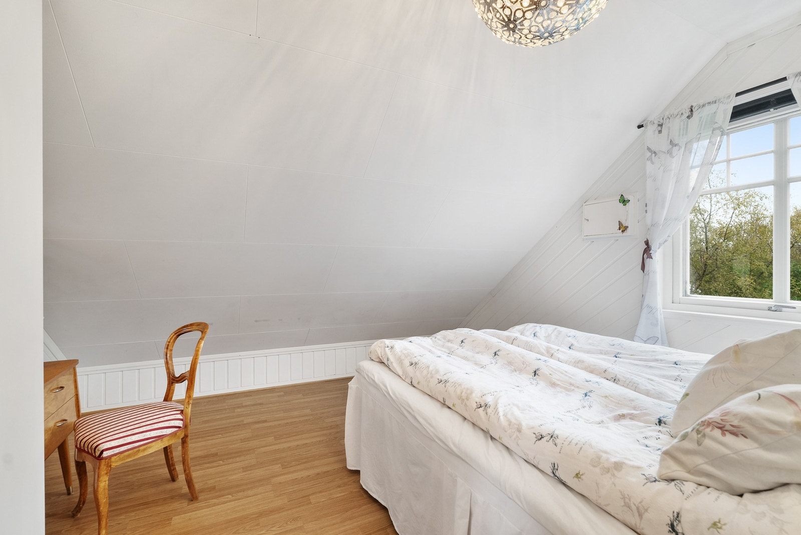 Soverom med skråtak, gulvbelegg og vindu mot landlige omgivelser. Galleribilde