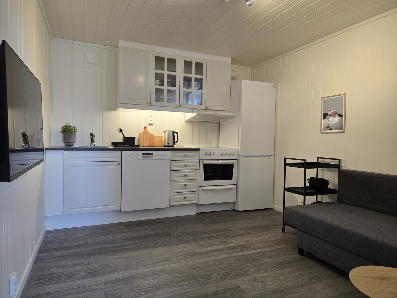 Kjøkkenet er innredet med med profilerte fronter og vitrineskap samt frittstående komfyr, oppvaskmaskin og kjøleskap med fryser. Galleribilde