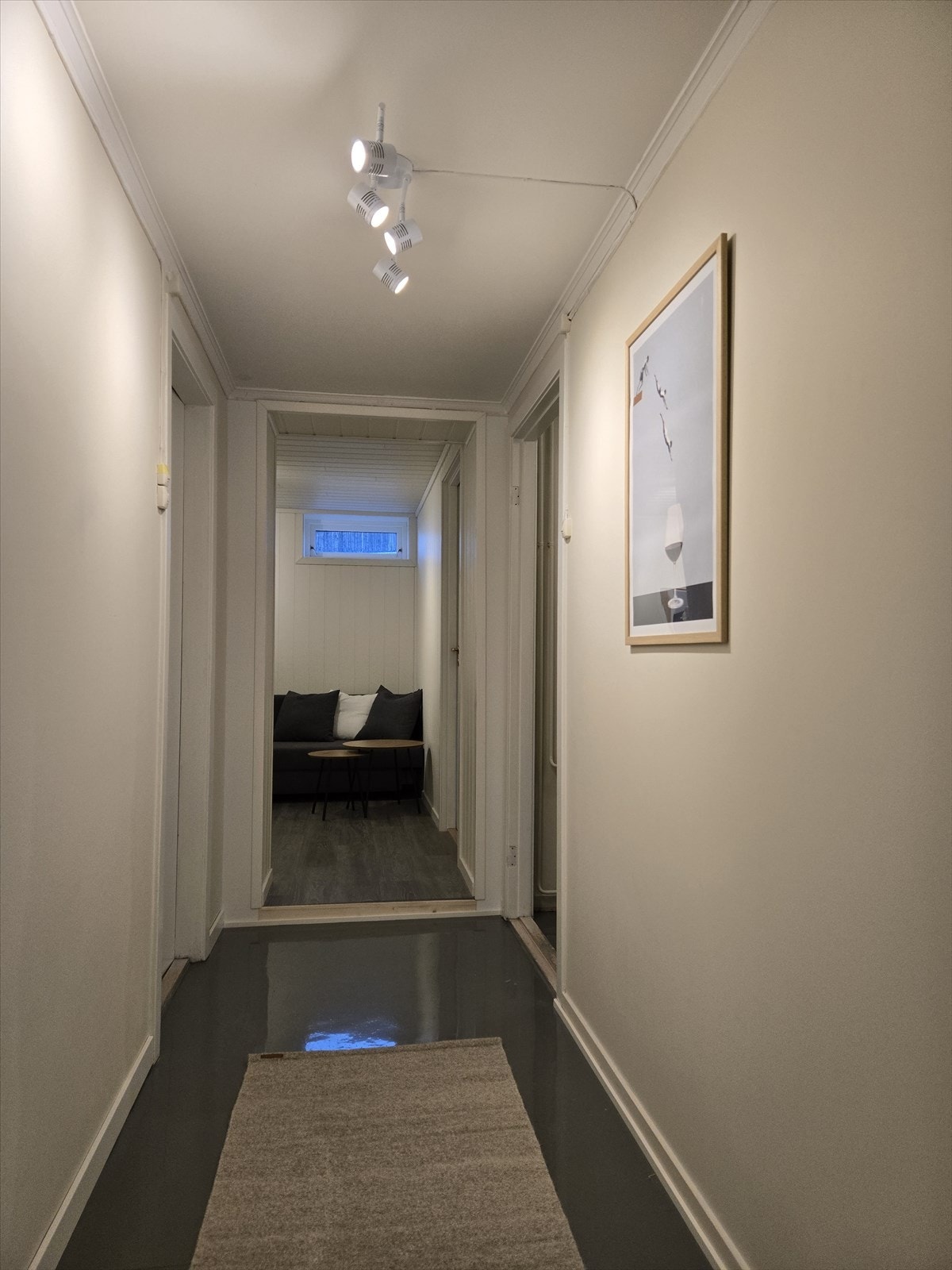 Langstrakt gang som knytter rommene sammen. Spotbelysning i taket og vindu gir godt lys i gangarealet. Galleribilde
