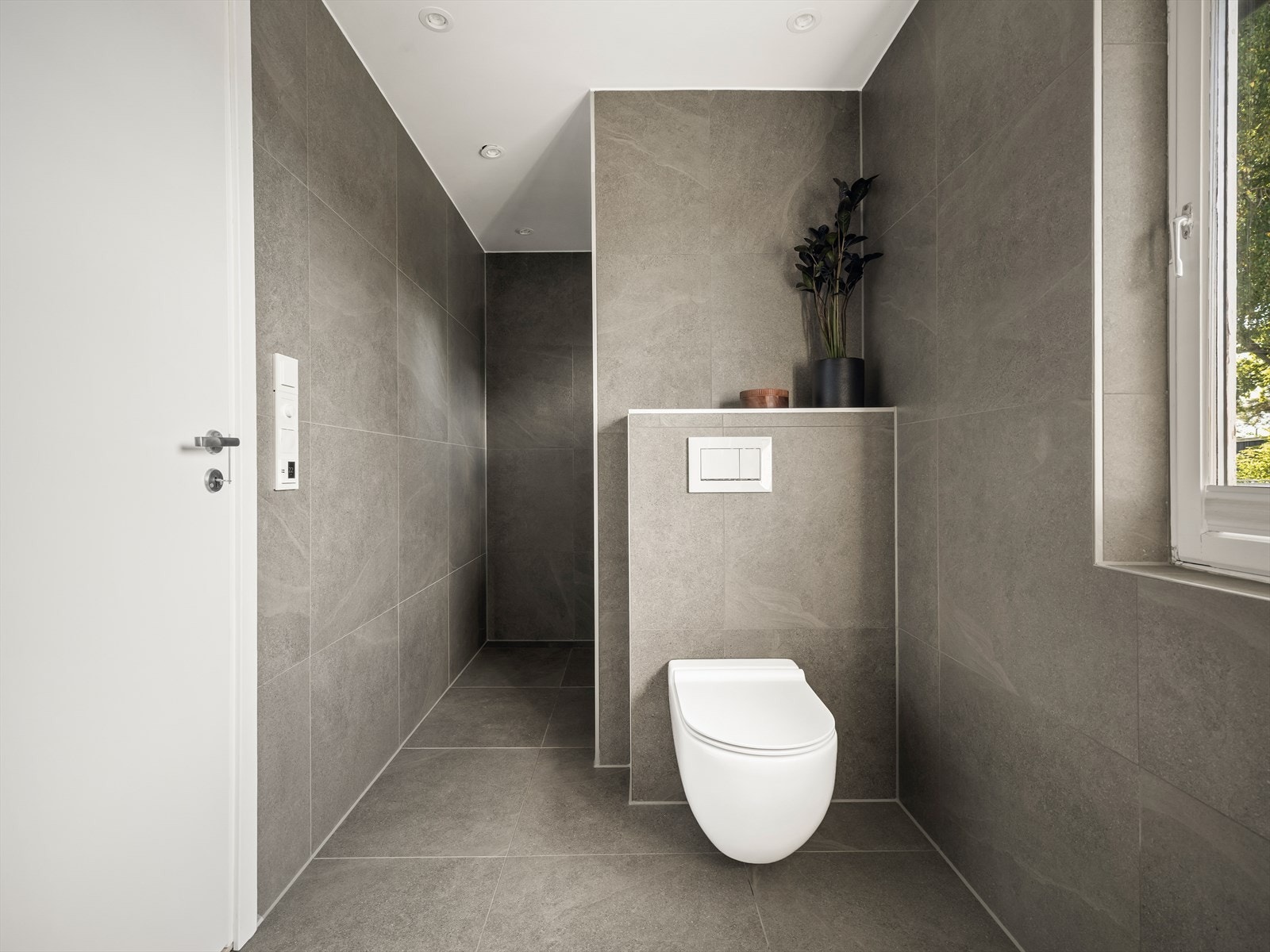 Badet har et moderne og gjennomført uttrykk med store fliser, gulvvarme og vegghengt toalett. Galleribilde
