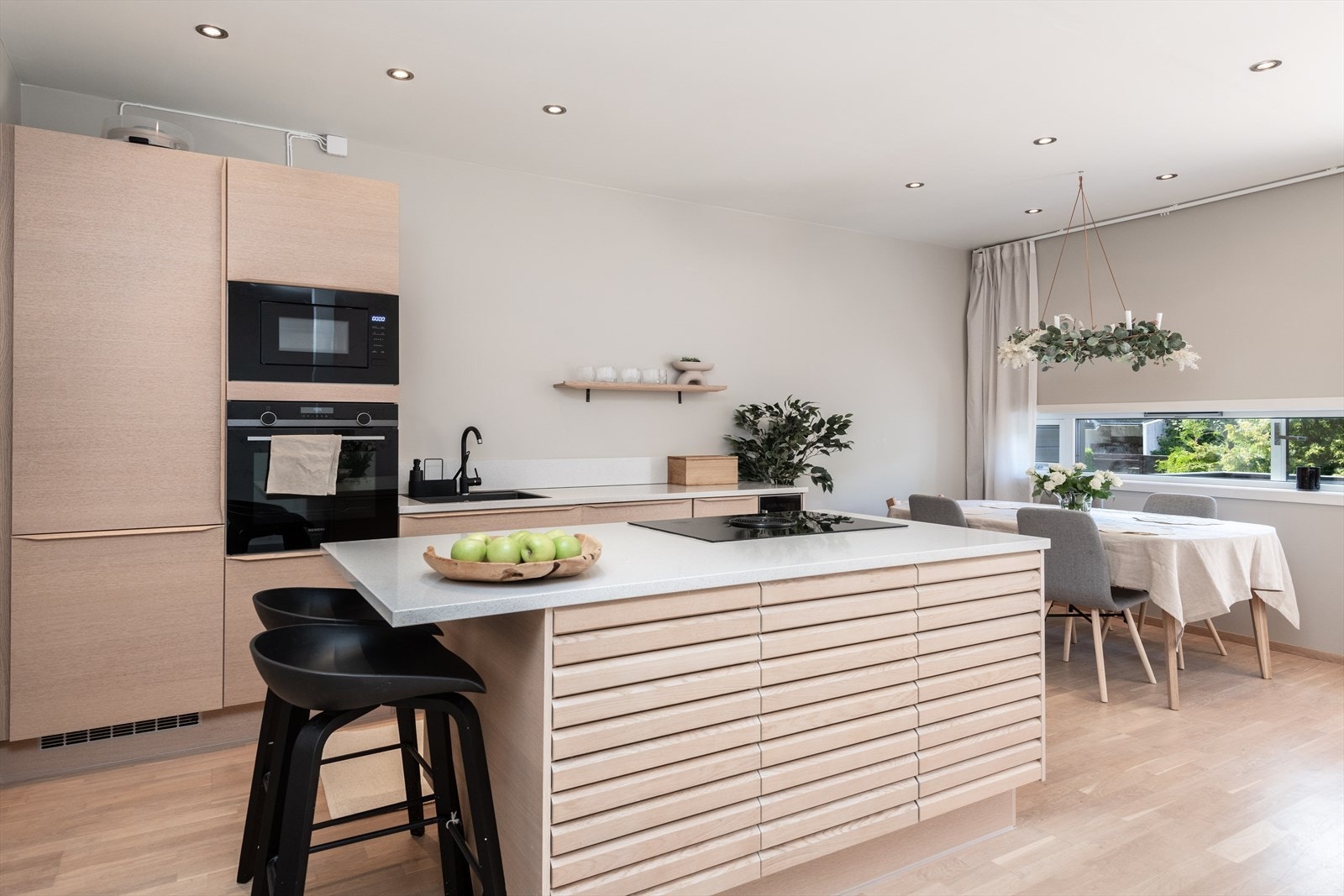 Kjøkkenet fra 2019 fremstår elegant og nordisk, med hvite steinbenkeplater og elegante eikefronter og skuffer. De sorte, integrerte hvitevarene inkluderer platetopp med nedtrekk og et vinskap. Galleribilde
