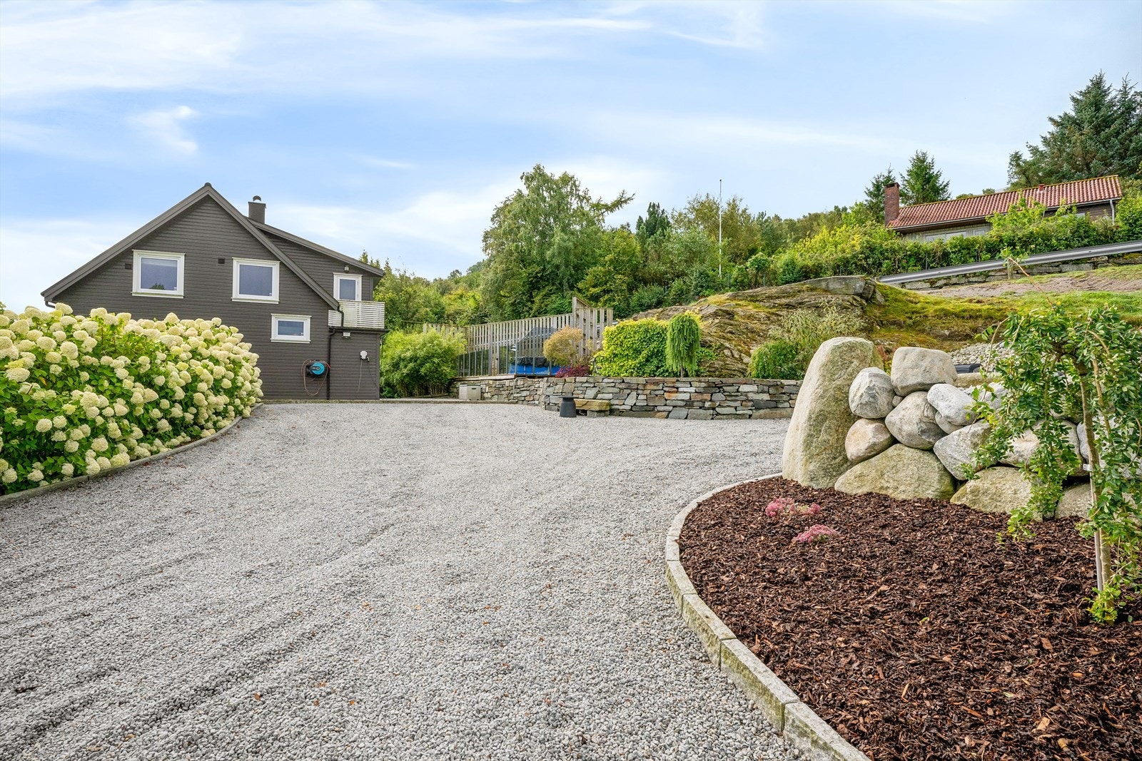Romslig gruset gårdsplass med god plass til biloppstilling og opparbeidede beplantningsfelt. Galleribilde