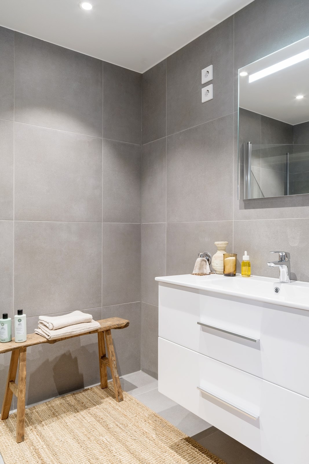 Badet er innredet med servant i skuffeseksjon, speil med belysning, vegghengt toalett og dusjsone med innfellbare glassdører. Galleribilde