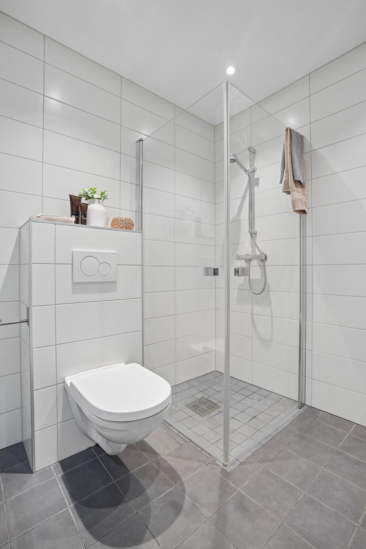 Badet er ustyrt med vegghengt toalett med drensutløp og dusjhjørne med glassdører. Galleribilde