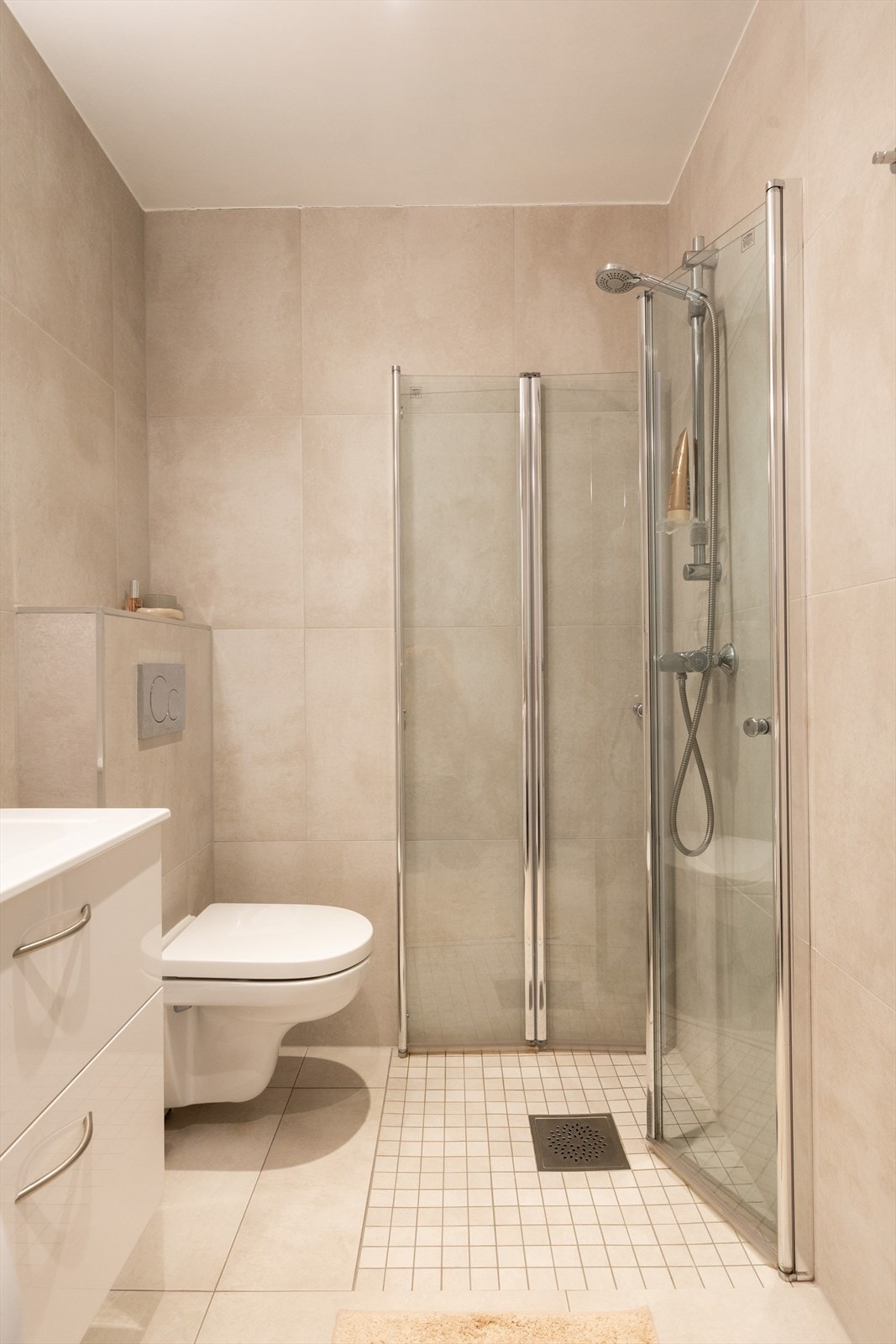 Badet er innredet med vegghengt servant med underskap, speil med belysning, vegghengt toalett og dusjhjørne med glassvegger. Galleribilde