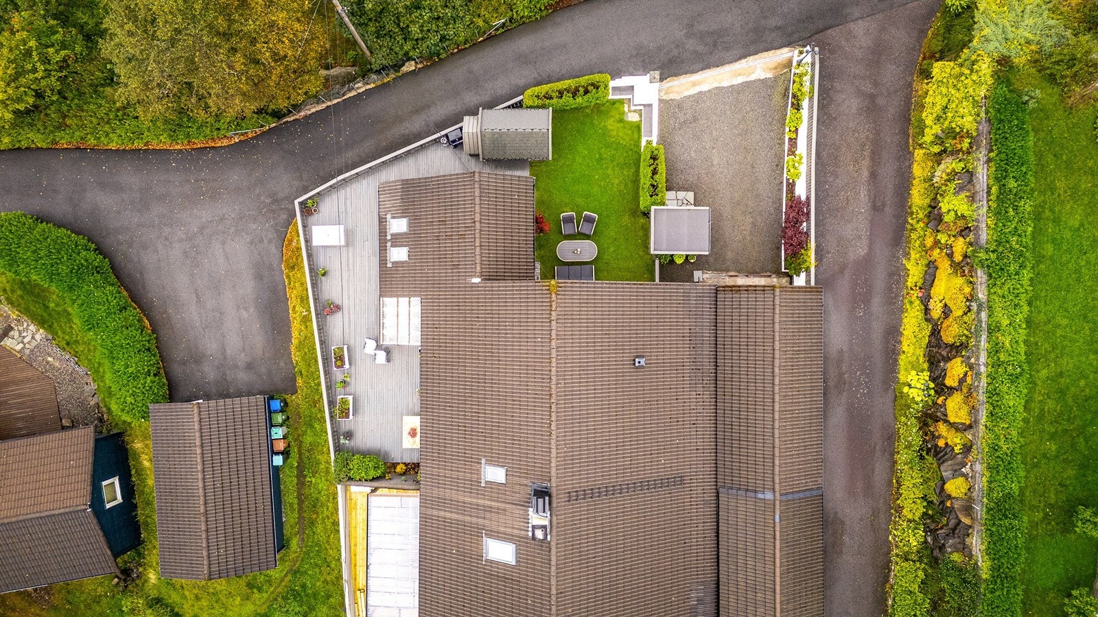 Droneoversikt over eiendommen - Pent opparbeidet tomt med treterrasser, gressplen og innkjørsel. Galleribilde