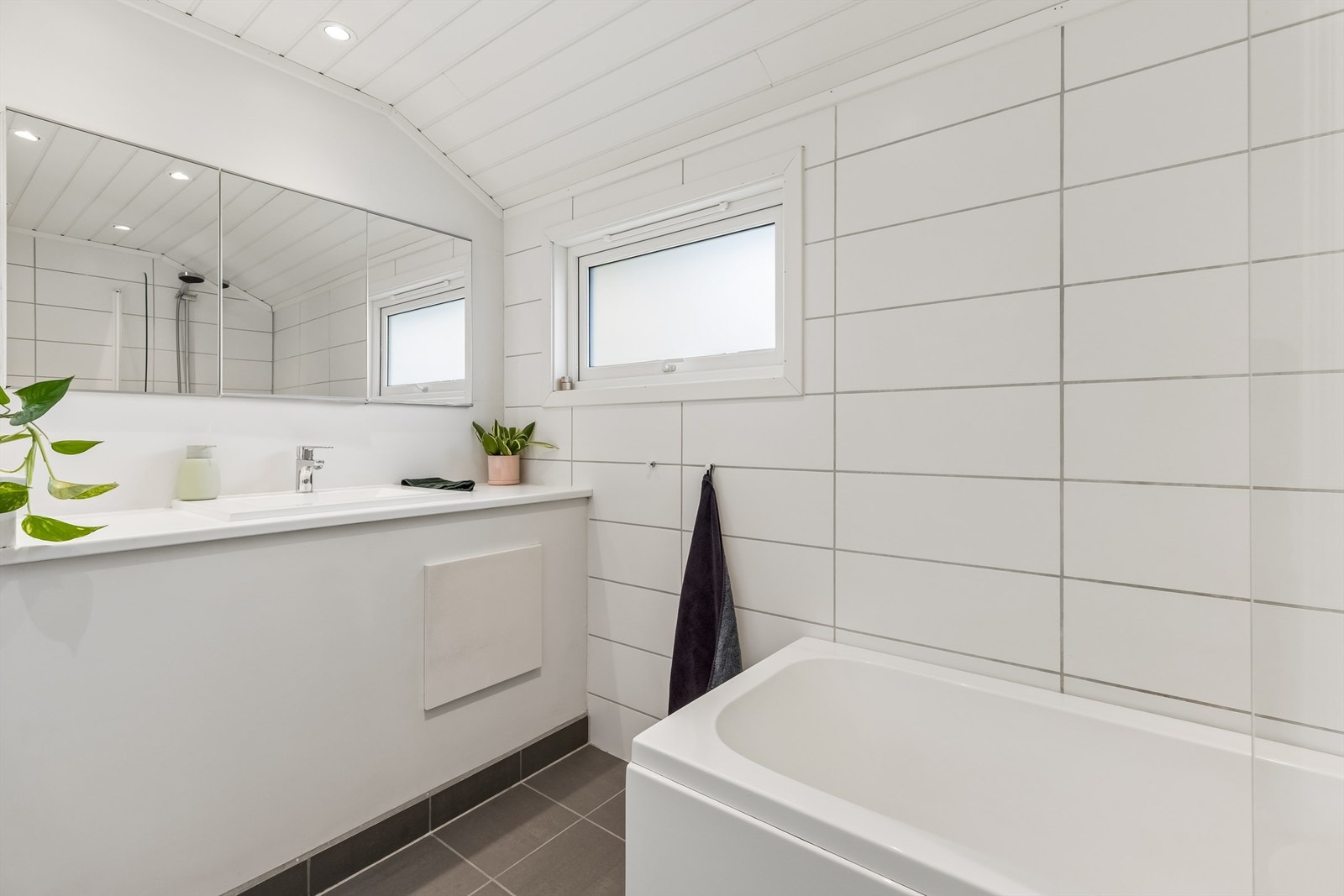 Pent baderom med flislagte vegger- og gulv med gulvvarme, samt skråtakshimling i MDF-paneler med downlights. Galleribilde