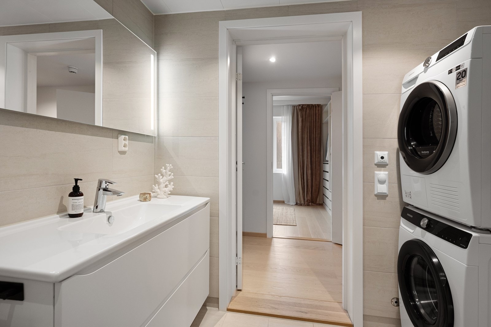 Videre har badet et vegghengt toalett, opplegg for vaskemaskin og et dusjhjørne med innfellbare glassdører. Det er opplegg for vaskemaskin, varmekabler i gulvet og downlights i himlingen. Galleribilde