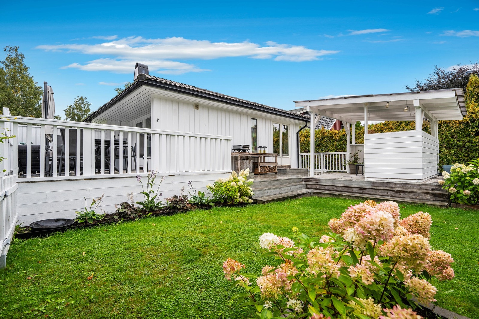 Innbydende og pent opparbeidet uteområde med romslig terrasse, overbygd uteplass og frodig hage. Galleribilde