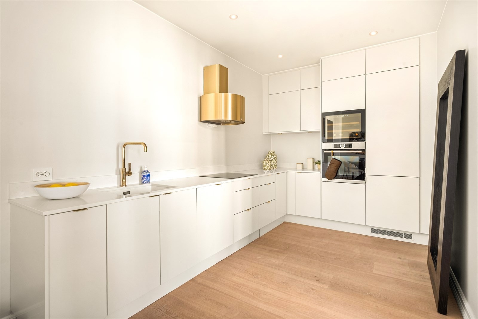 Påkostet kjøkken med kompositt benkeplate, Røros Luna kjøkkenhette i børstet messing, Bosch stekeovn, Franke pure vask og downlights i taket. Galleribilde