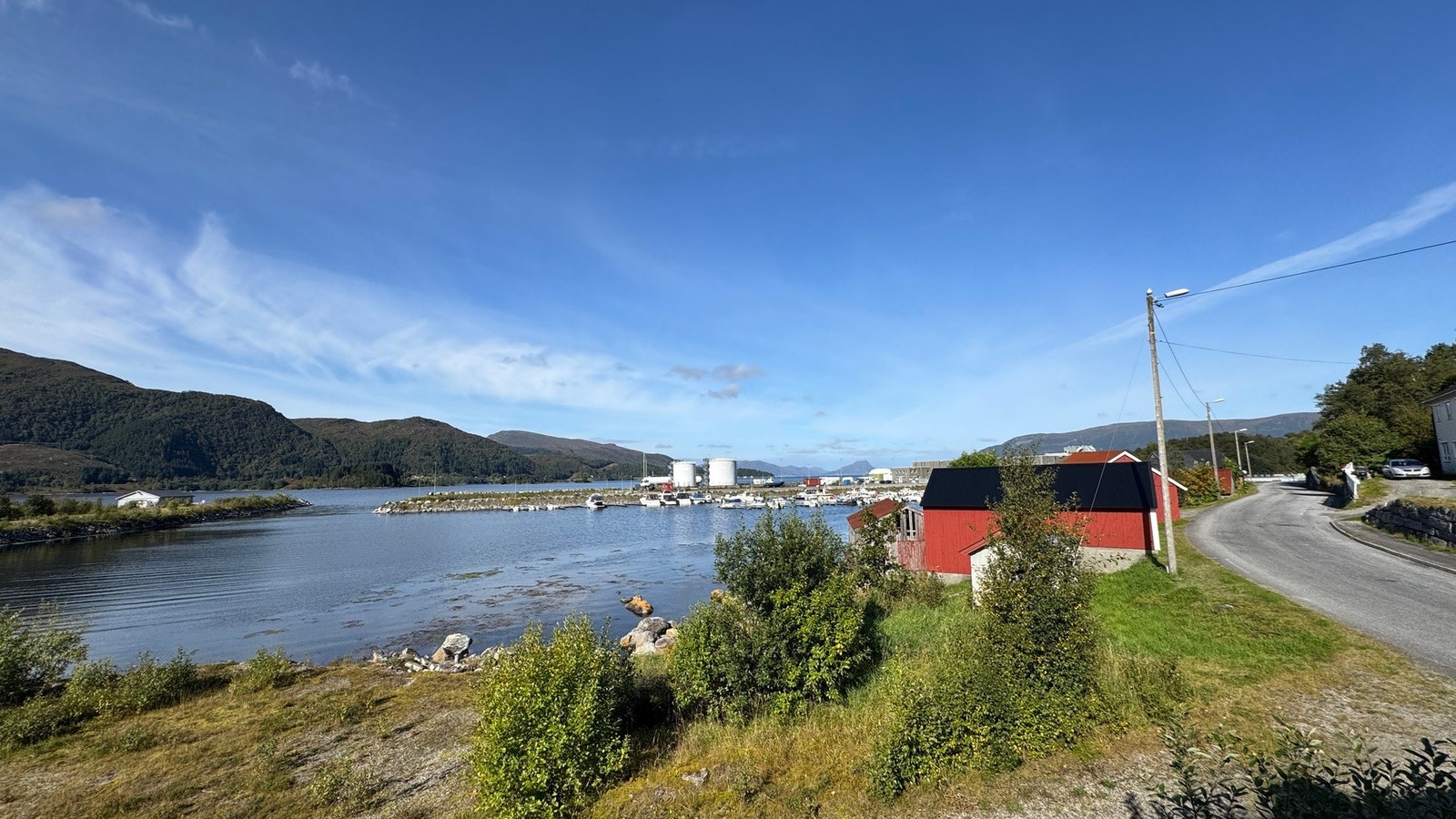 Utsikt over fjorden og småbåthamna, med fjella på motsett side. Galleribilde