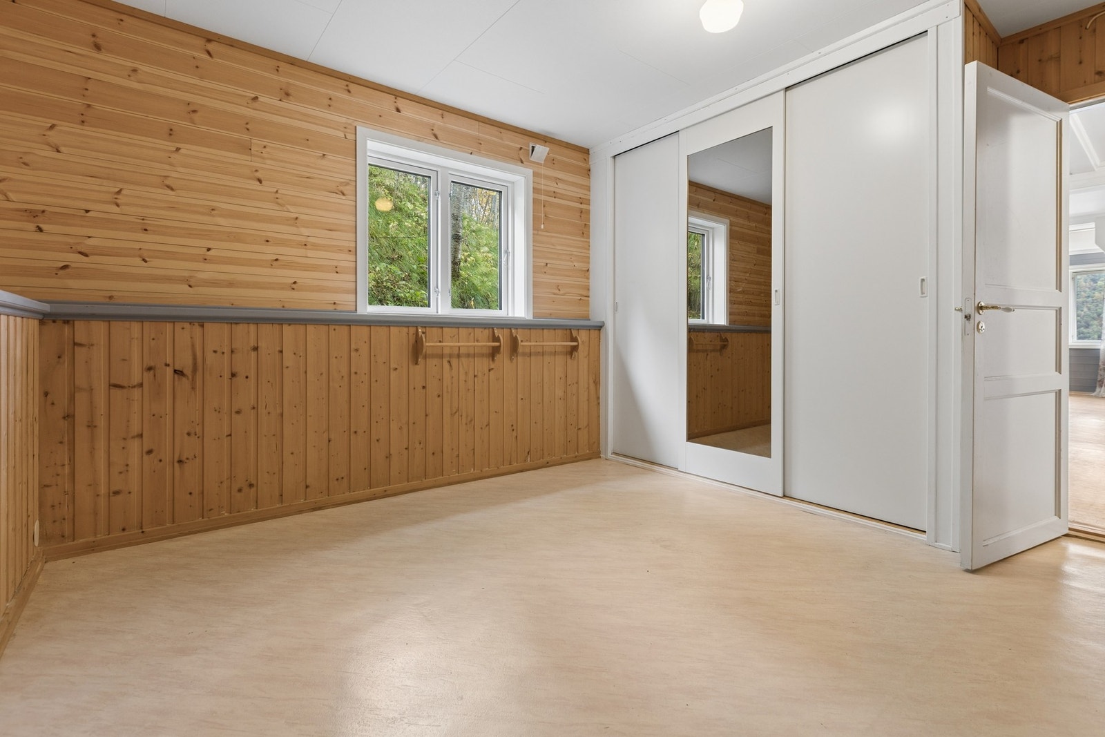 Soverom i hovedetasjen med trepanel på veggene og romslig skyvedørsgarderobe. Galleribilde