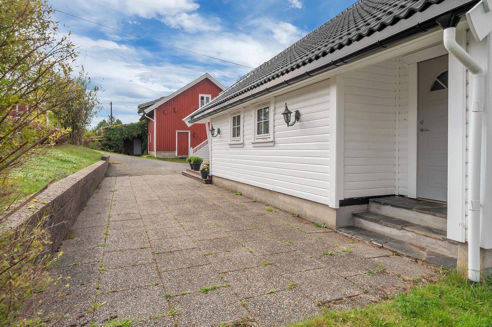 Hellelagt uteplass langs husveggen med trappeoppgang til inngangen. Galleribilde