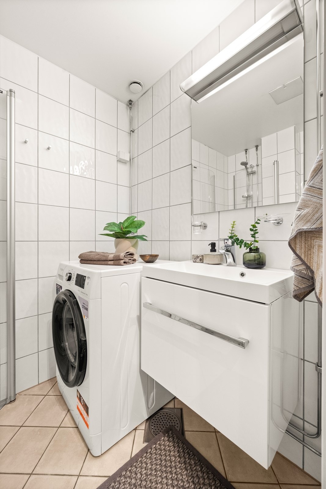 Badet er utstyrt med gulvstående toalett, dusjhjørne med innfellbare glassdører og baderomsinnredning med skuff, servant med ettgreps blandebatteri og speil med belysning. Galleribilde