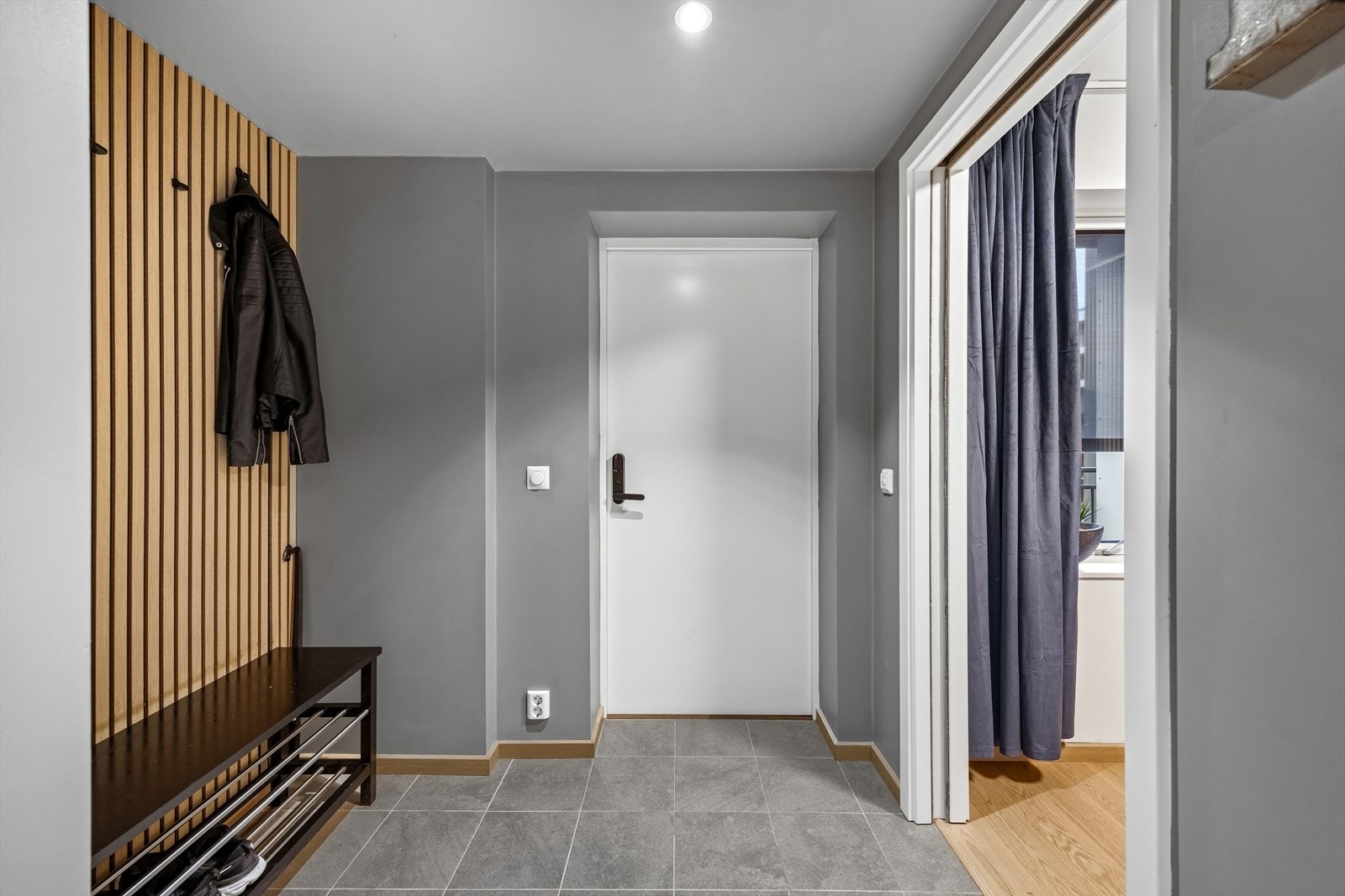 Velkommen inn - Leiligheten ønsker velkommen inn i en romslig og innbydende entré med fliser på gulv, dekorativ spilevegg og malte flater i moderne og stilrene fargetoner. Galleribilde