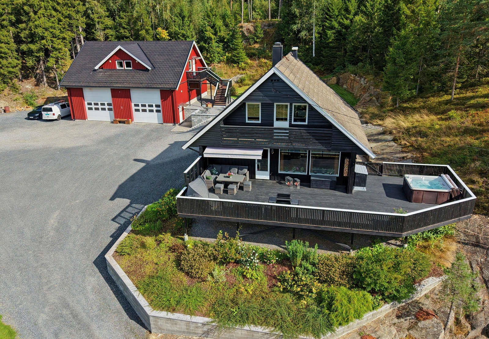 Bolig med stor terrasse, frittliggende garasje og romslig uteområde omgitt av skog. Galleribilde