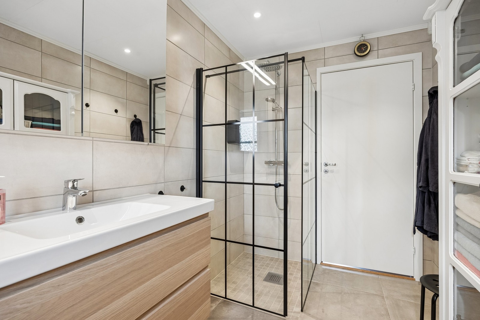 Badet er flislagt på både gulv og vegg, og fremstår med en moderne løsning med vegghengt klosett og romslig dusjhjørne - et stilrent og funksjonelt rom. Galleribilde