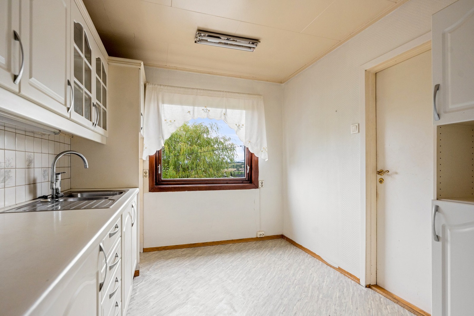 Kjøkken med hvit innredning og plass til spisebord ved vinduet. Galleribilde