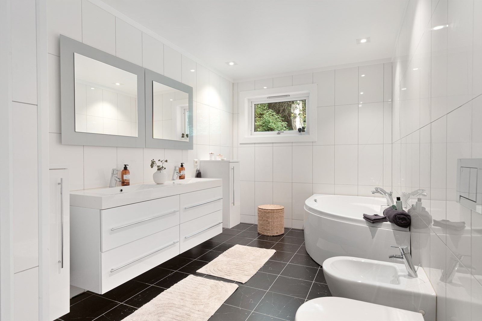 Eit romsleg bad med fliser på både golv og vegger og måla, slett himling. Badet har golvvarme og er innreidd med dusj, badekar, servantskap, speil/speilskap, vegghengt toalett med innbygd sisterne og bidé. Galleribilde
