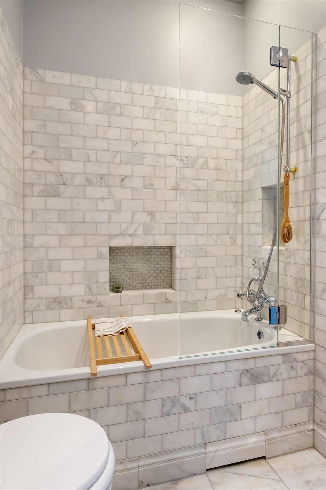 Badekar med dusjløsning og glassvegg, og en praktisk nisje til oppbevaring av dusjartikler. Galleribilde