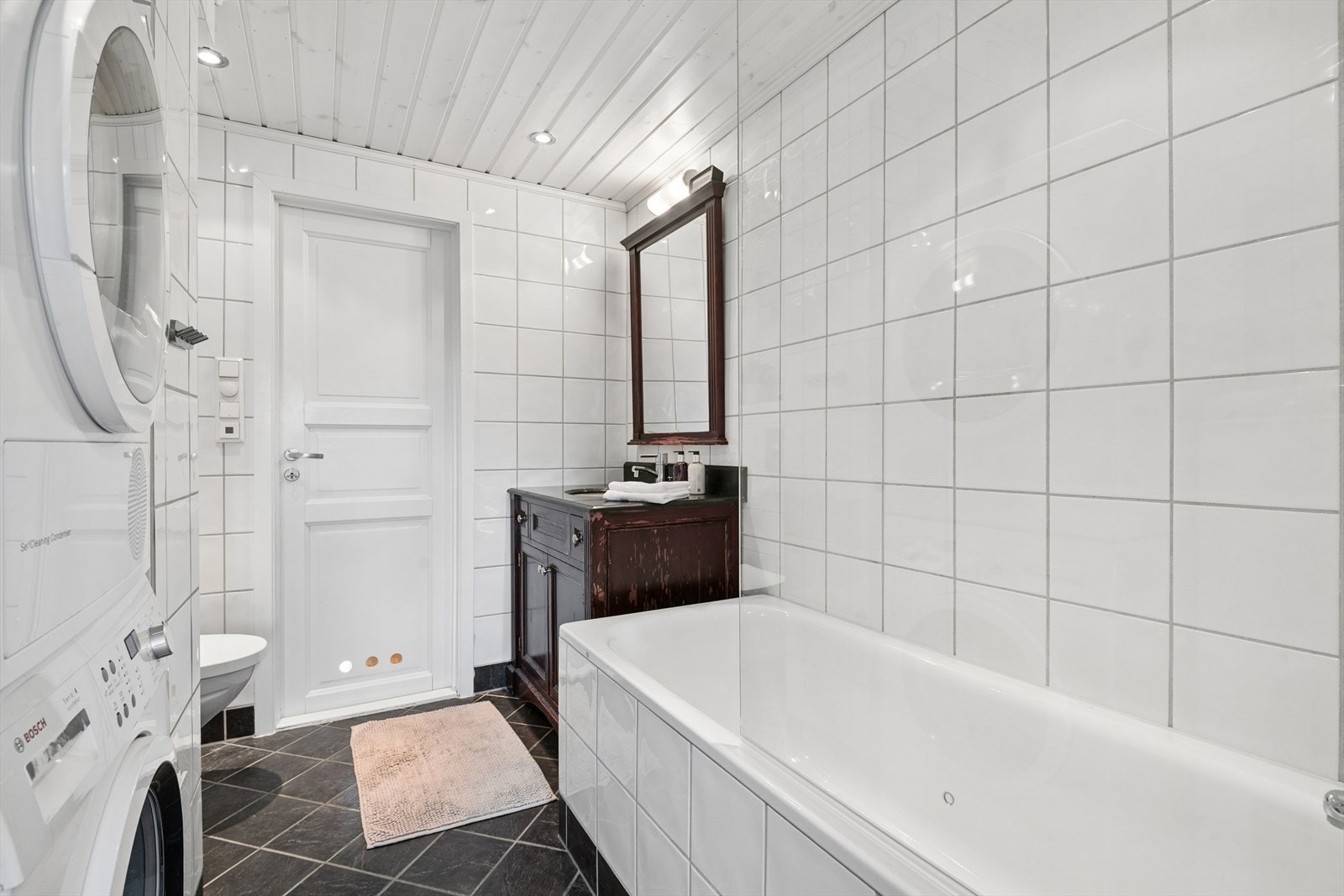 Hovedbadet har badekar, dusj, servant med skapinnredning, toalett og opplegg til vaskemaskin og tørketrommel Galleribilde