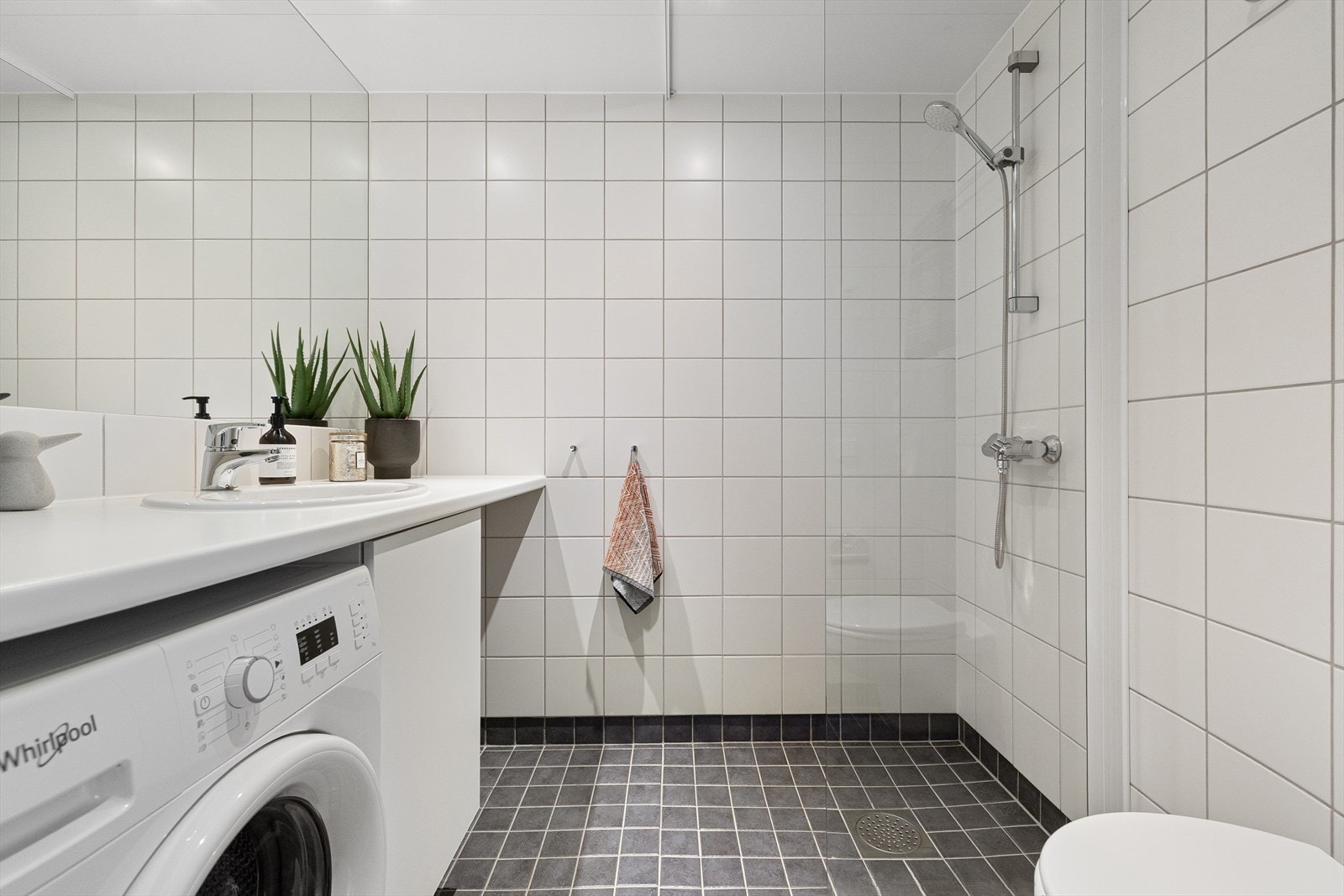 Badet innredet med servant, benkeplate, speil, vegghengt toalett og dusj. Galleribilde