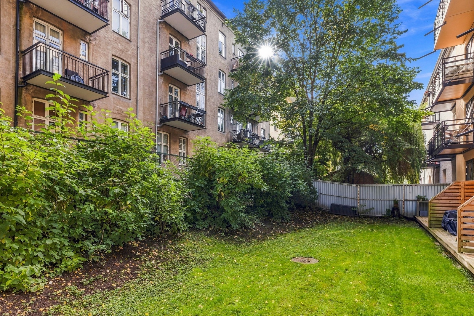 Mellom bygårdene ligger et grønt gårdsrom med plen og frodig beplantning. Galleribilde