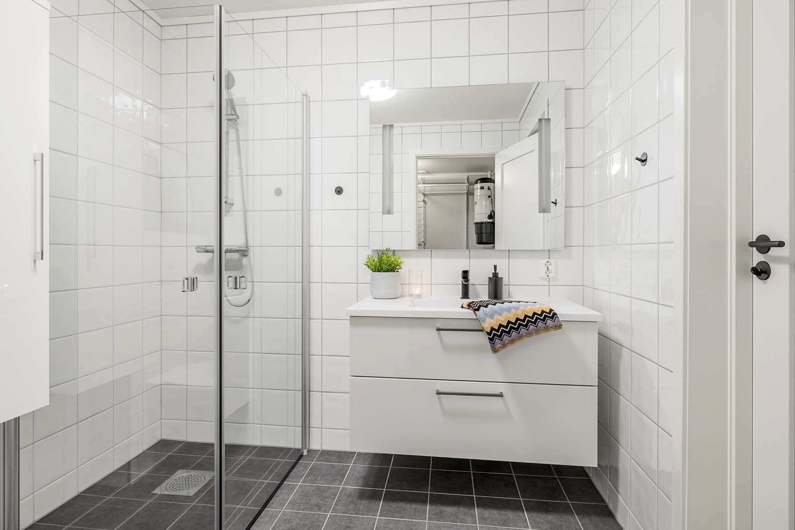Hvit baderomsinnreding med glatte fronter og skuffer med ovenpåliggende servant med ett-greps armatur. Speil med sidelys over servant Galleribilde