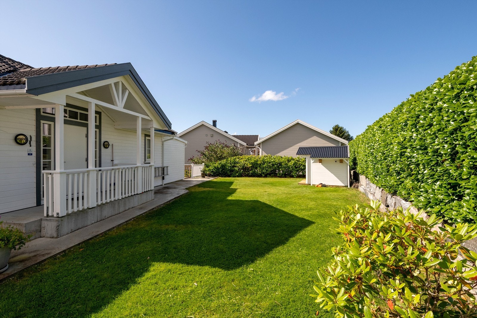 Skjermet hage omkranset av tett hekk og et lite frittstående uthus på tomten. Galleribilde