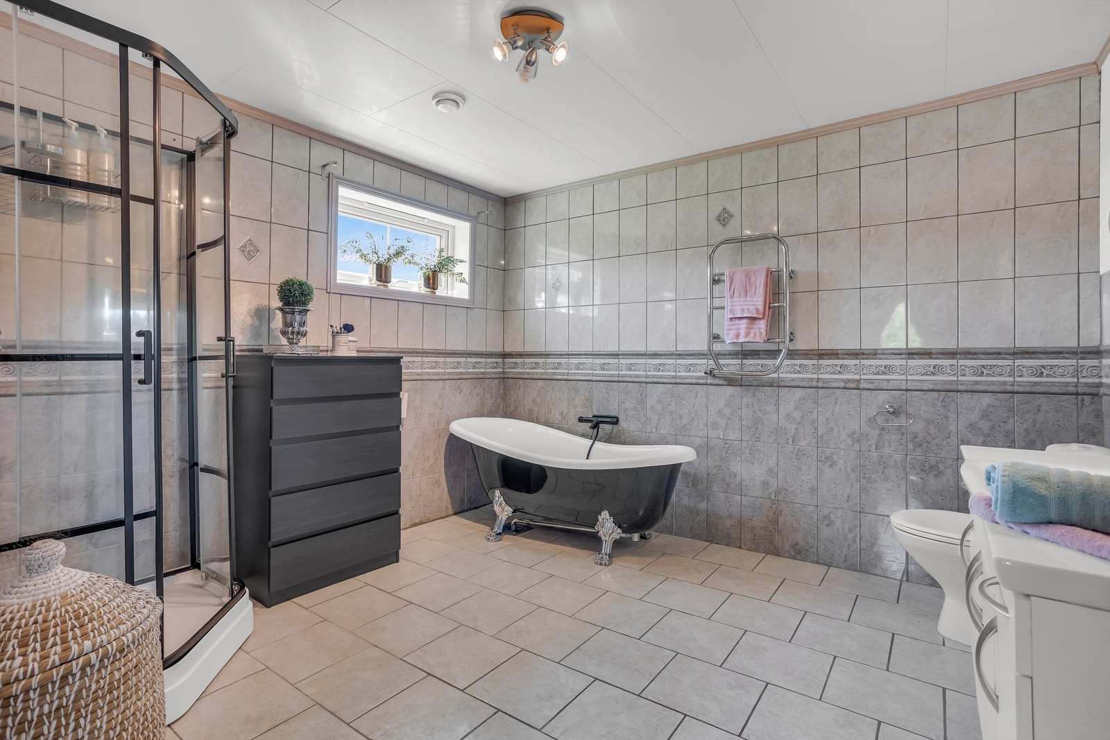 Badet er bestående av toalett, heldekkende servant i innredning, speil med belysning, badekar og dusjkabinett med skyvedører. Galleribilde