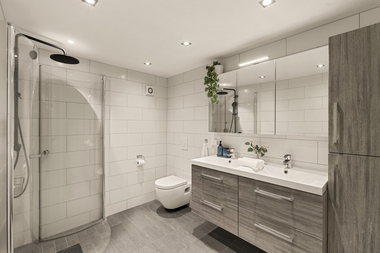 Badet er innredet med 2 nedfelte servanter, veggmontert toalett og dusjhjørnet. Flislagt gulv med varmekabler. Galleribilde