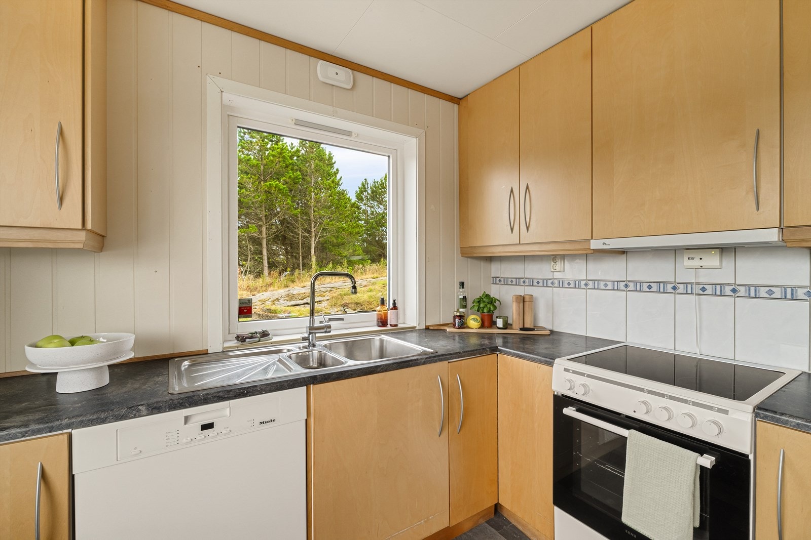 Innredningen har finerte fronter og laminert benkeplate, med flislagt vegg mellom benkeplate og overskap. Galleribilde