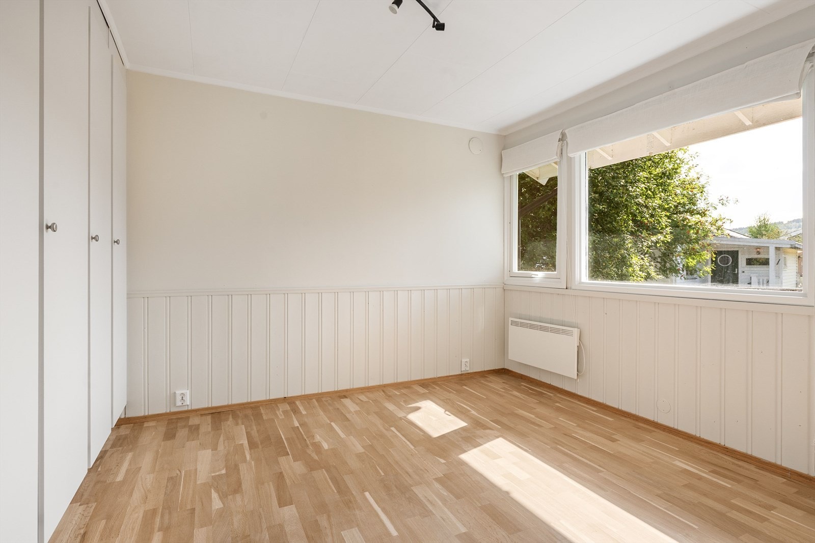 Stort og lyst soverom i 1.etasje med plassbygde garderobeskap på en vegg. Galleribilde