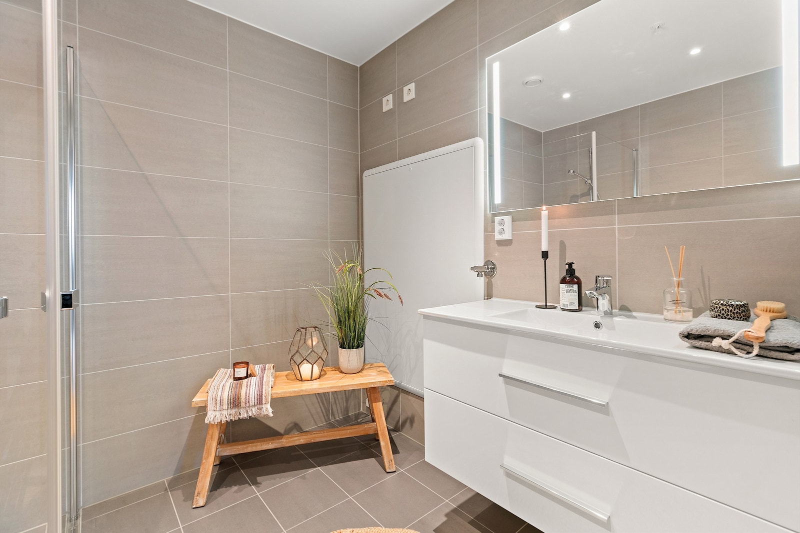 Badet har et moderne og stilrent uttrykk med store veggfliser i formatet 30 x 60 cm og matchende gulvfliser i 30 x 30 cm. Galleribilde