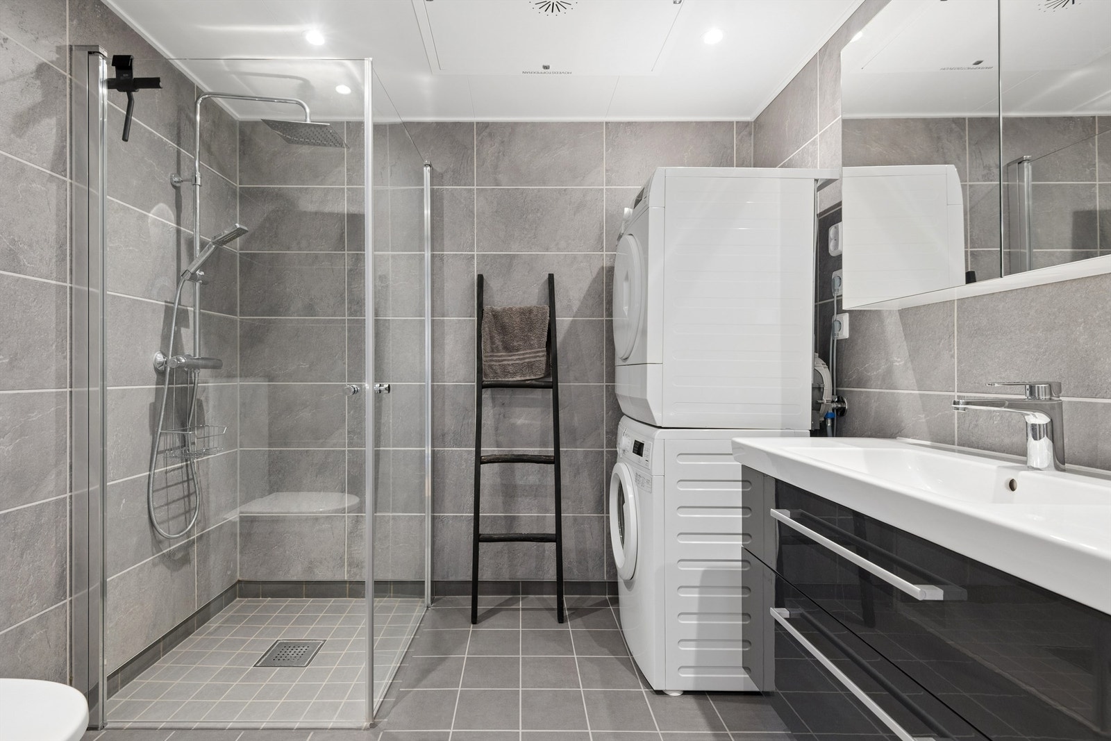 Badet har flislagte gulv og vegger, samt gulvvarme. Det er innredet med servant, speilskap, dusjhjørne med både hånddusj og regndusj, vegghengt toalett og opplegg for vaskemaskin. Galleribilde