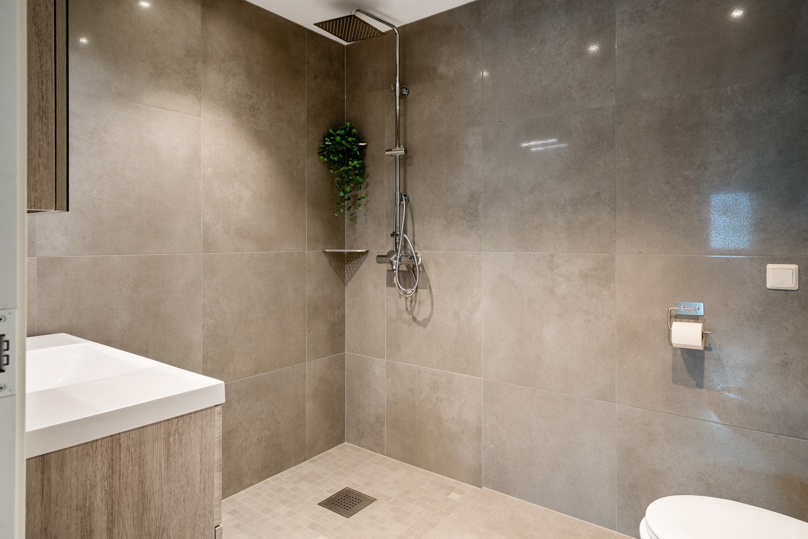 Badet har rikelig med plass til toalettartikkel og håndklær i servantskap og overskap. Åpen dusjsone med mulighet for å etablere dusjdører om man ønsker det. Galleribilde