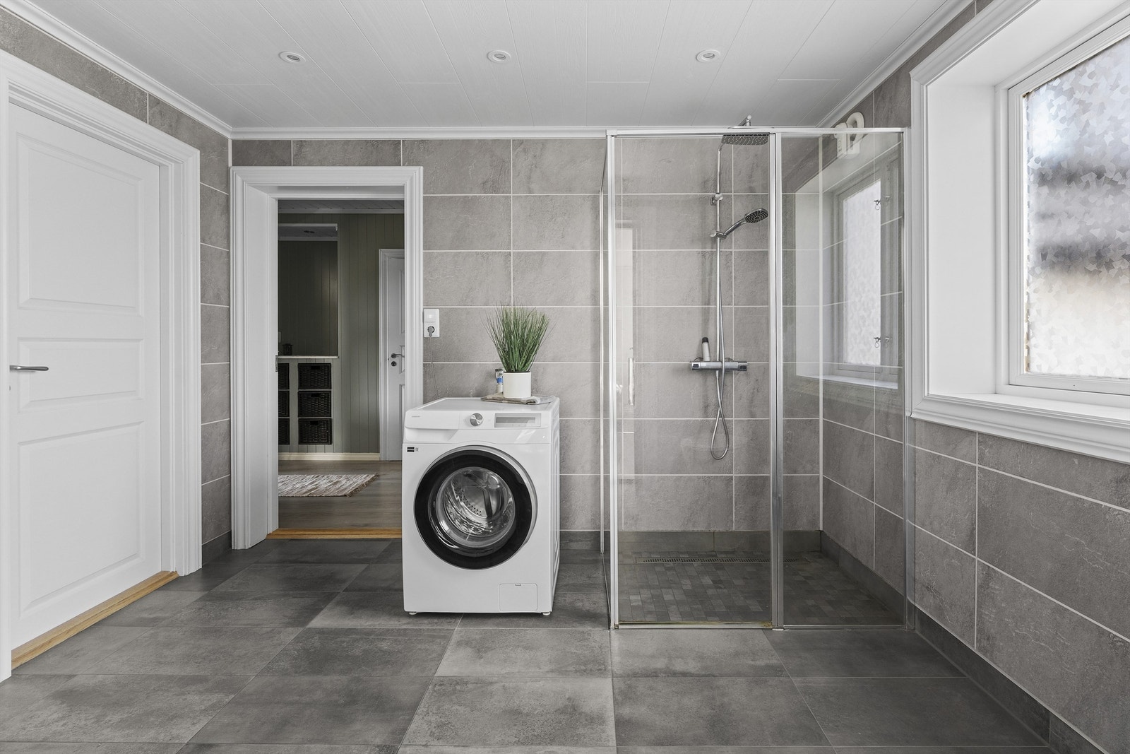 Badet er innredet med vegghengt servantskap med skuffer, speilskap med overlys, dusj på gulv og vegghengt toalett med innebygget sisterne. Galleribilde