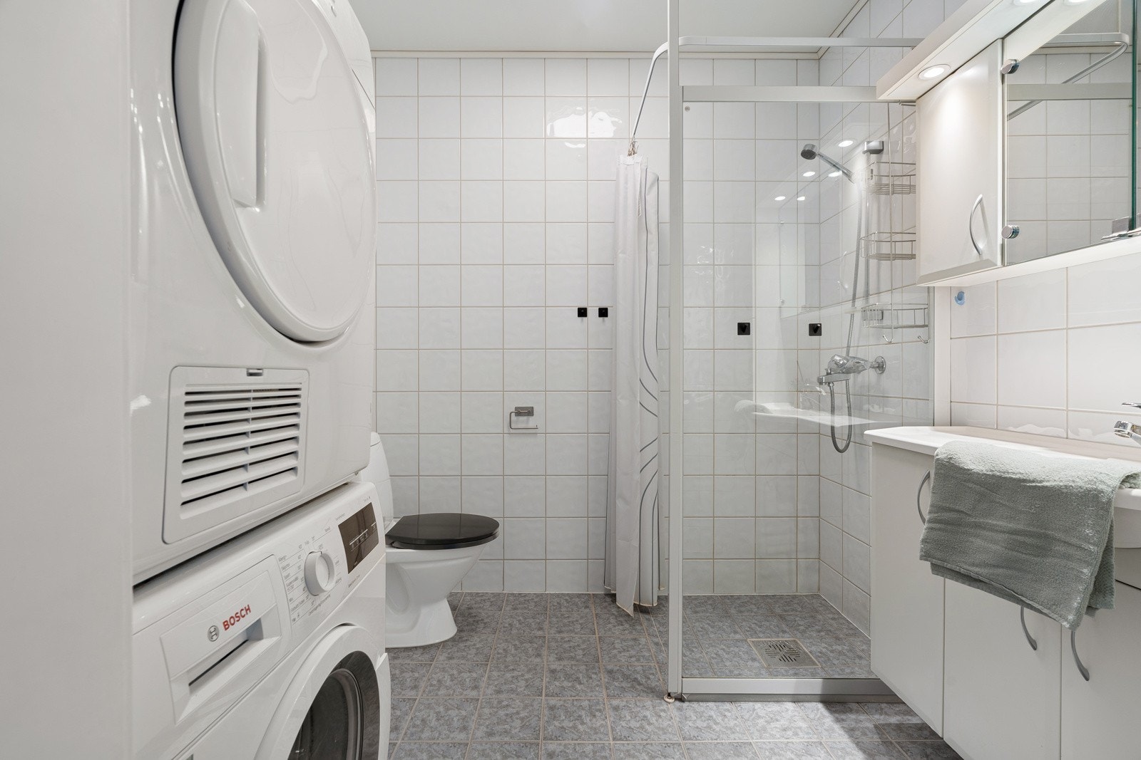 Flislagt bad/wc/vaskerom med vannbåren gulvvarme, baderomsinnredning med servant og speil, samt dusjhjørne.