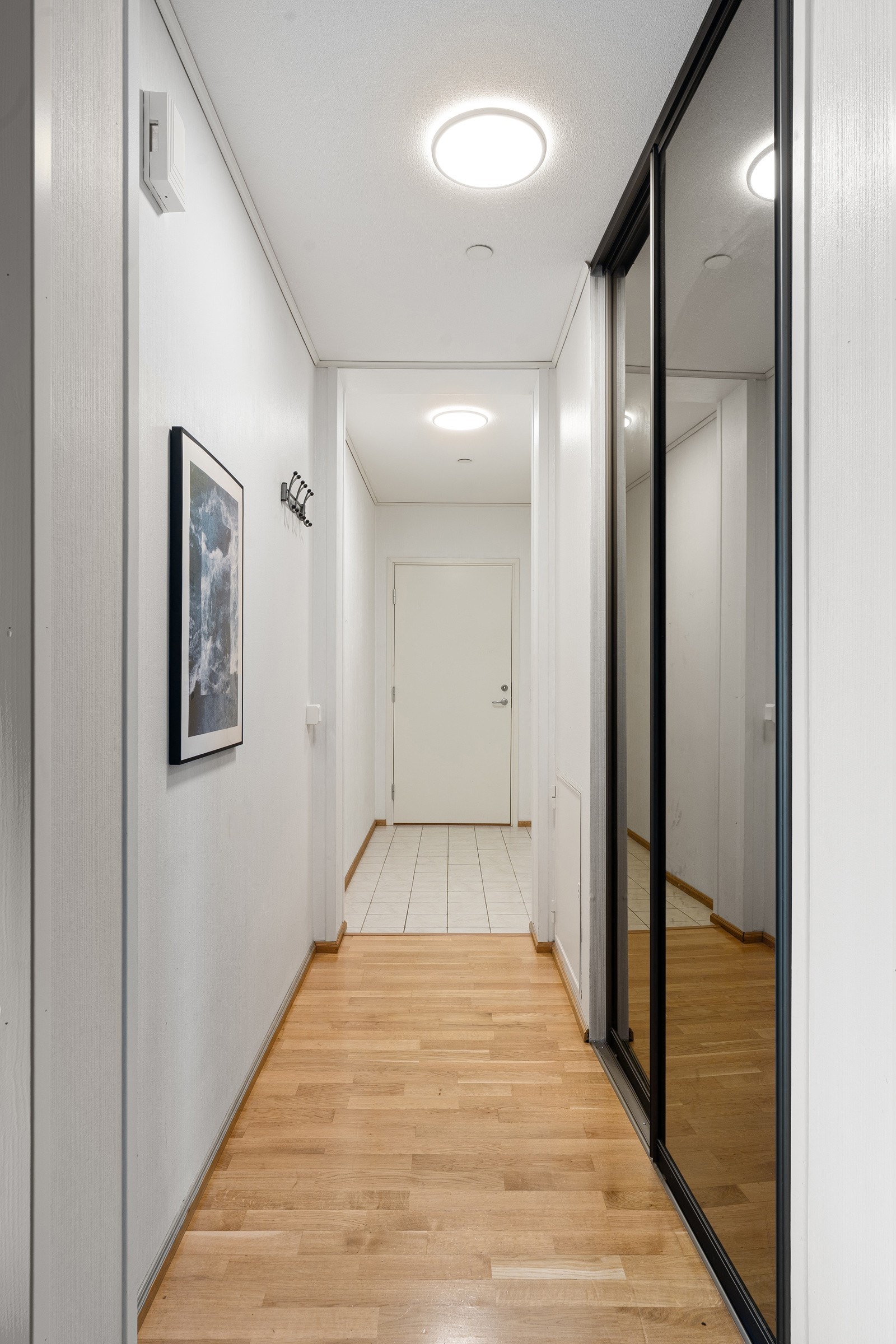 Gang med parkettgulv og romslig skyvedørsgarderobe som gir god oppbevaringsplass for yttertøy og sko.