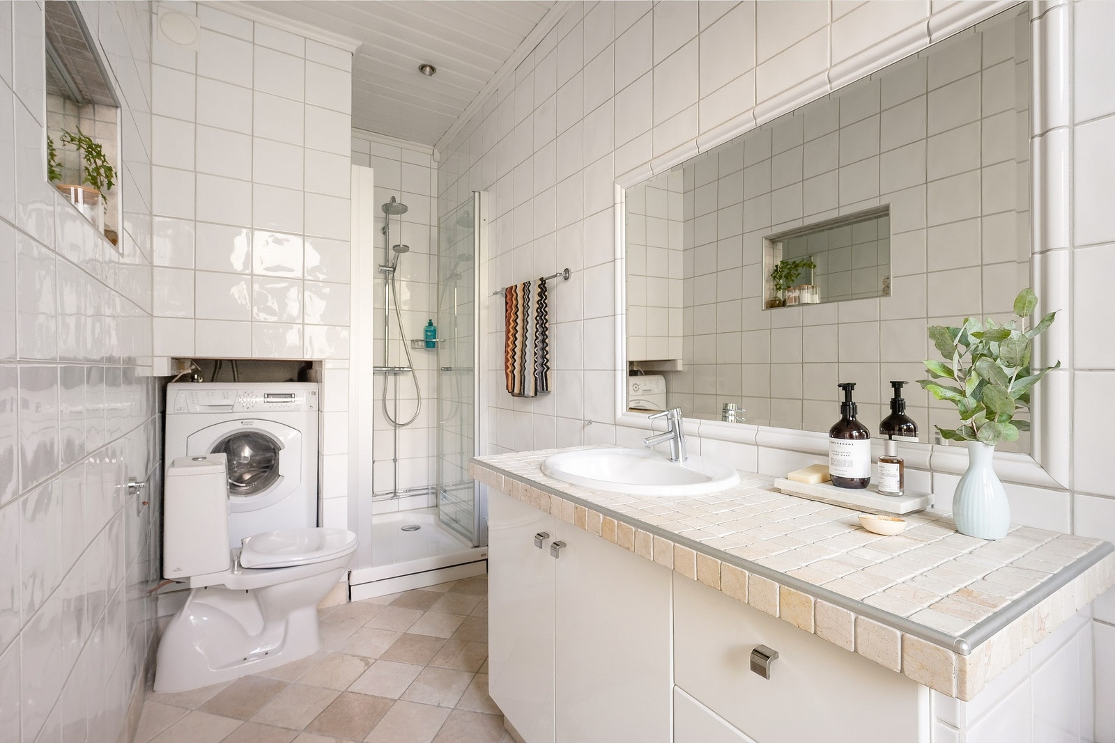 Badet er innredet med gulvstående toalett og dusjkabinett i nisje med vegghengt dusjarmatur og glassdør Galleribilde