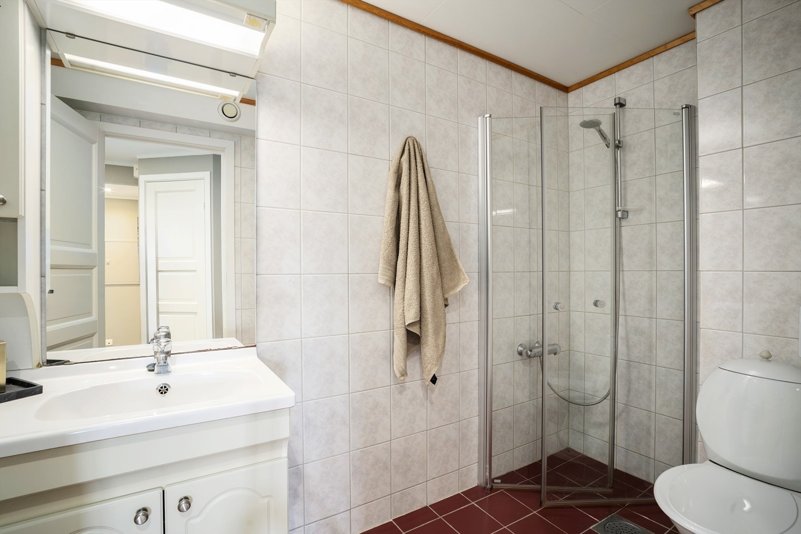 Badet er innredet med lys, profilert baderomsinnredning med servant og speil, gulvmontert toalett samt dusjnisje med innfellbare glassdører. Galleribilde