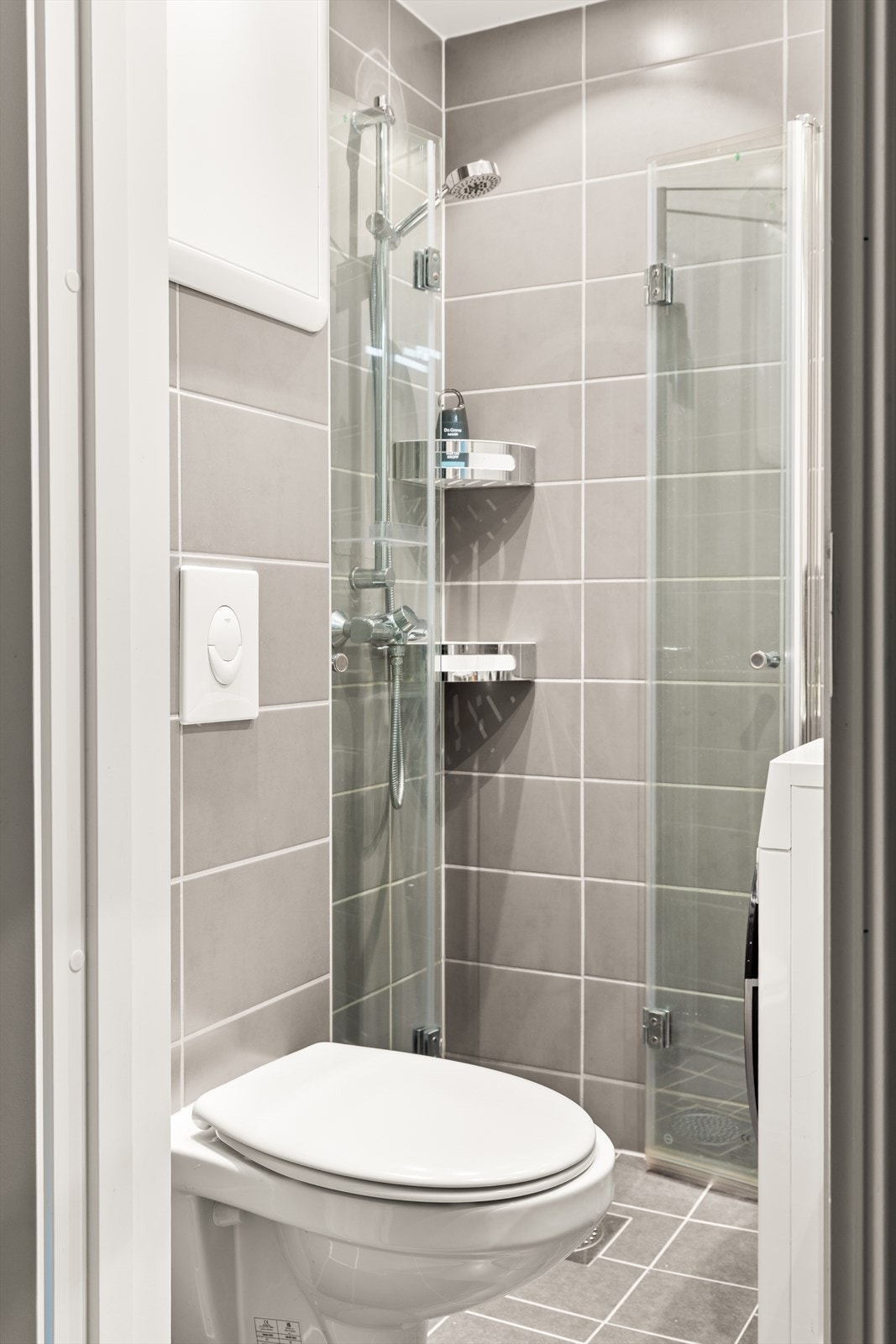 Badet er flislagt på gulv og vegger og har servant med skuffer under, dusj, toalett og opplegg for vaskemaskin Galleribilde